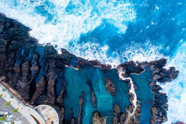 Bovenaanzicht van de natuurlijke vulkanische zwembaden van Porto Moniz, waar helderblauw oceaanwater tegen zwarte rotspartijen slaat.