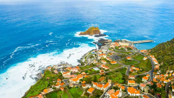 Een panoramisch aanzicht op het kuststadje Porto Moniz met witte huizen met oranje daken, gelegen op een rotsachtige landtong langs de ruige, blauwe Atlantische Oceaan op Madeira.