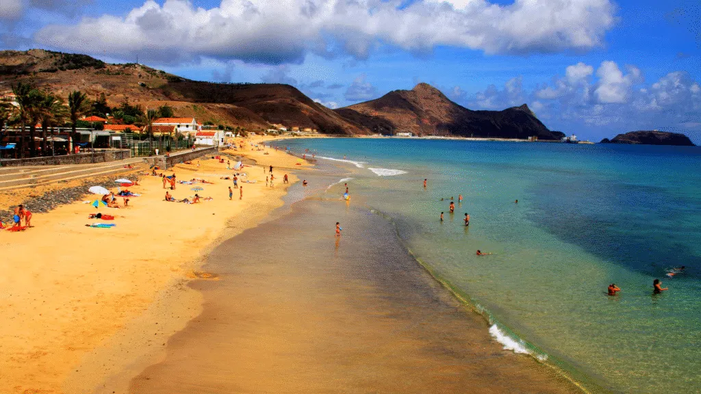 Breed goudgeel zandstrand met mensen in het heldere, turkooizen water en heuvels op de achtergrond op het eiland Porto Santo bij Madeira