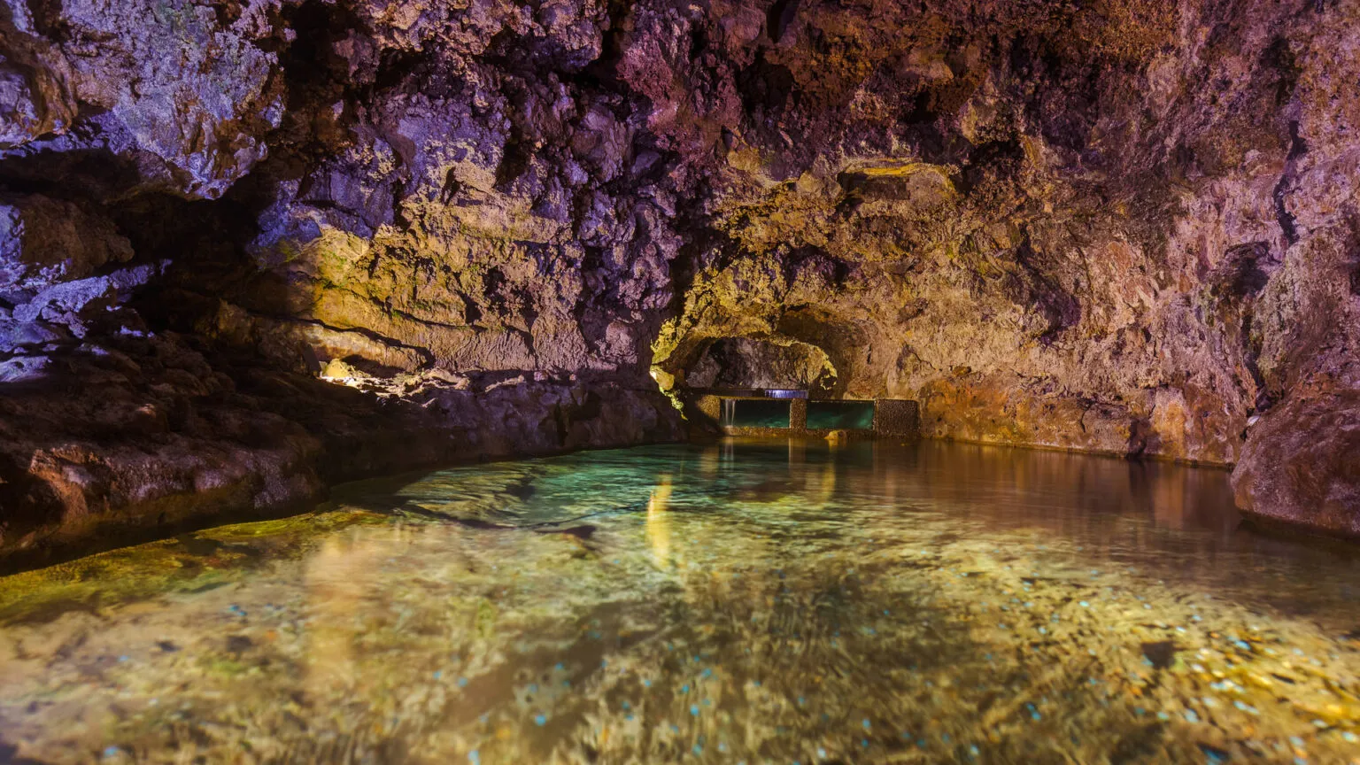 Een verlicht ondergronds waterreservoir omgeven door ruige lavasteen in de vulkanische grotten van São Vicente op Madeira.
