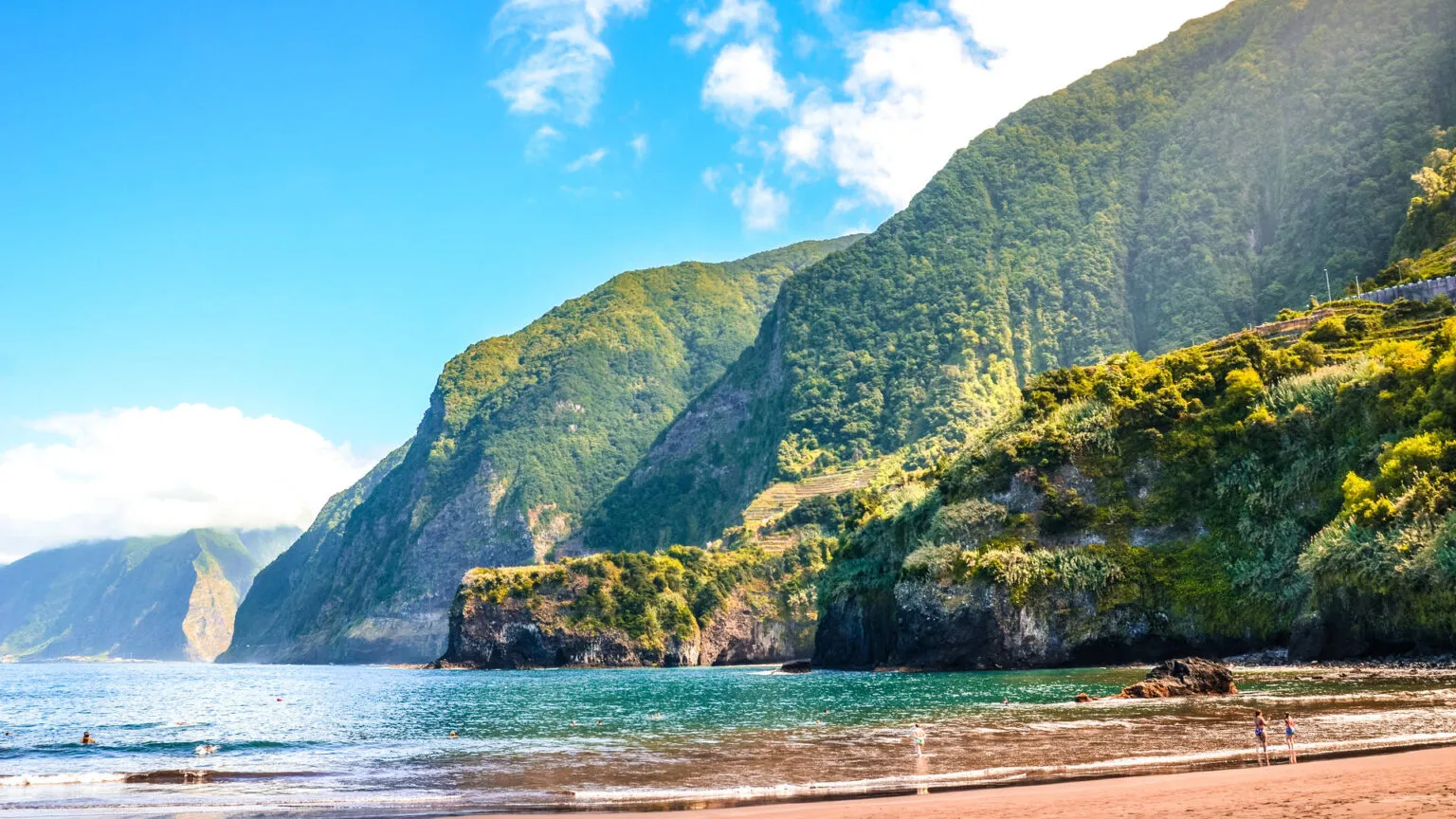 Het natuurlijke zwarte vulkanische strand van Seixal op Madeira, begrensd door imposante, groen begroeide bergkliffen en de Atlantische Oceaan.