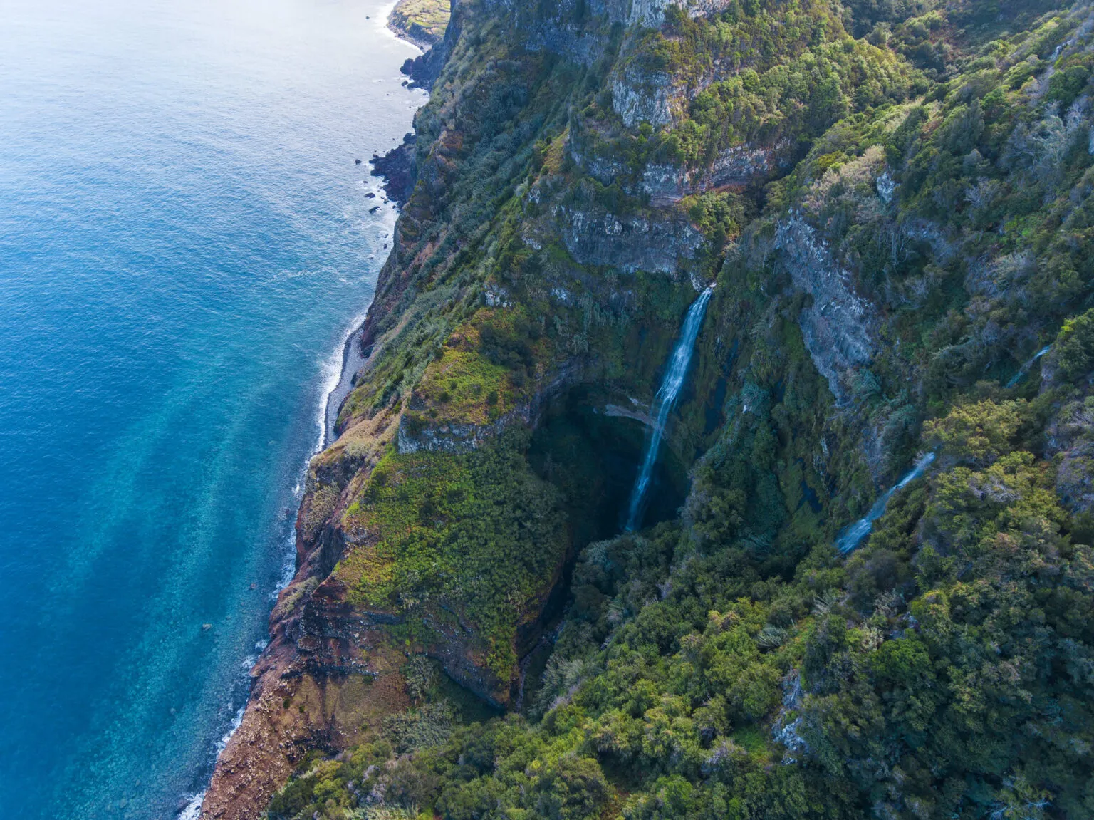 Hoge waterval stort langs een steile, groenbegroeide klif rechtstreeks neer in de Atlantische Oceaan op Madeira