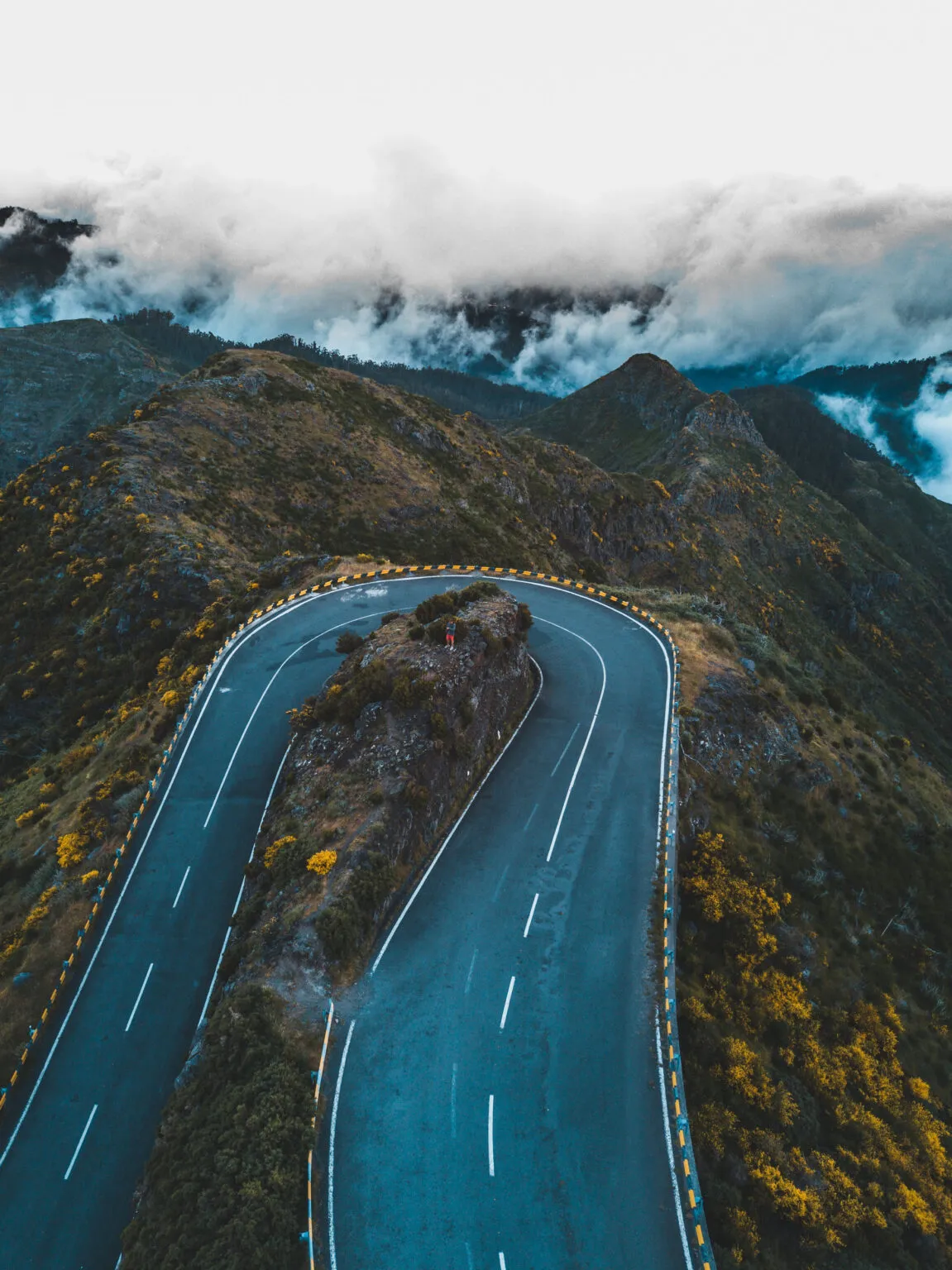 Scherpe bocht op een geasfalteerde weg tussen de ruige bergen en wolken op Madeira.