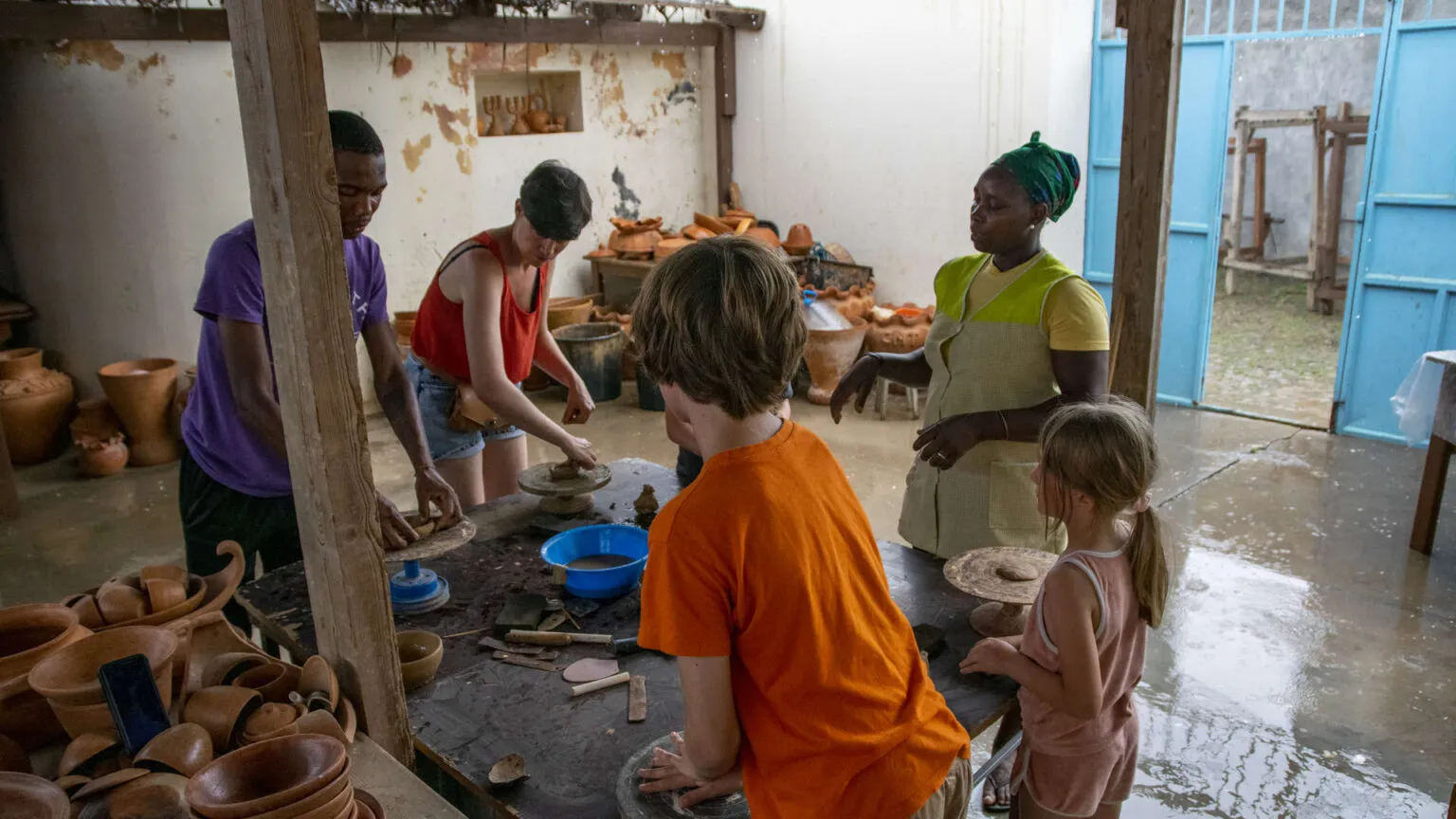Een jongen in het oranje en zijn gezin nemen samen met een lokale begeleidster deel aan een ambachtelijke workshop binnen op Kaapverdië.