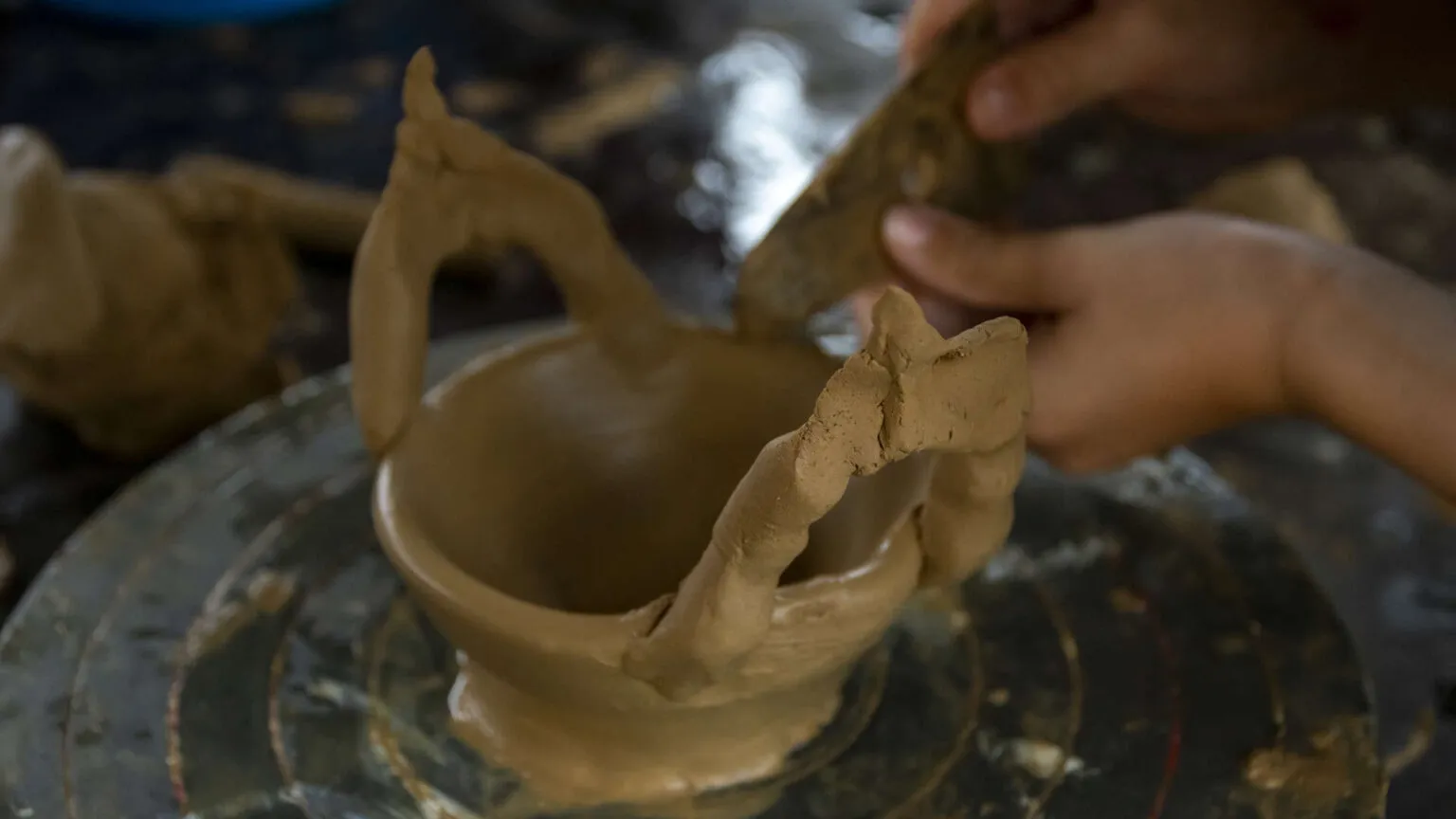 Close-up van handen die zorgvuldig een kleipotje vormen en bewerken tijdens een workshop op Kaapverdië.