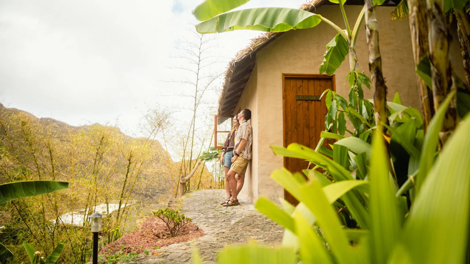 Twee reizigers ontspannen bij een traditioneel huisje omringd door tropische planten bij accommodatie Aldeia Manga op Santo Antão, Kaapverdië.