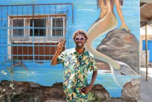Een vrolijk lachende local steekt twee vingers op voor een muur met kleurrijke streetart in hoofdstad Mindelo van eiland São Vicente