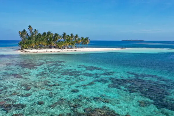 Aanzicht van een klein tropisch eilandje met palmbomen en een wit zandstrand, omgeven door helder, turkoois water in de San Blas-archipel van Panama.