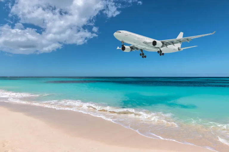 Wit vliegtuig vliegt over turquoise gekleurde zee en wit zandstrand, Maho Bay, Sint Maarten.