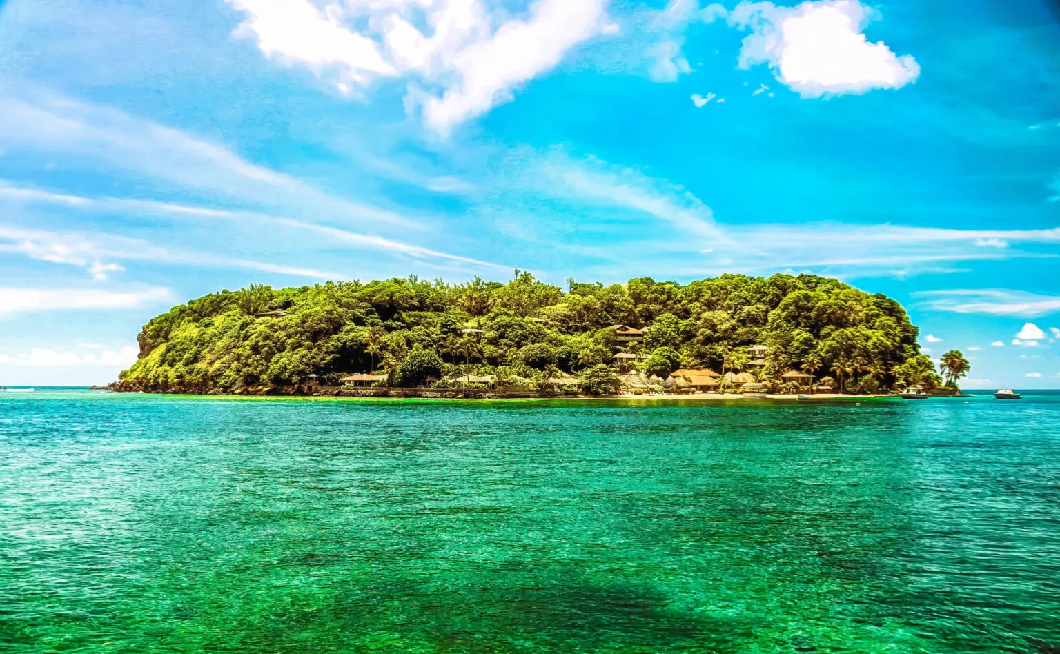 Zicht op het heldere turquoise-groene water van de Tobago Cays met een dichtbegroeid, groen eilandje op de achtergrond onder een felle blauwe lucht met lichte wolken.