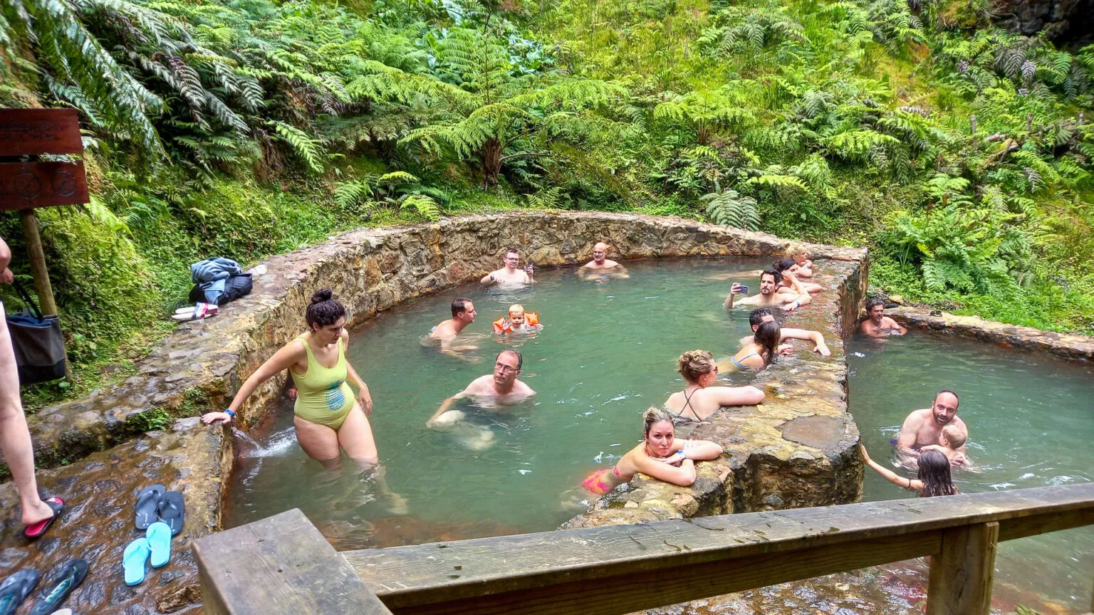 Reizigers ontspannen in het warme, ijzerrijke water van een natuurlijk thermisch bad omgeven door weelderige groene vegetatie in Caldeira Velha op São Miguel, Azoren.