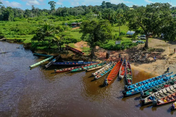 Luchtfoto van een rij lange, kleurrijke korjaal-boten die zijn aangemeerd aan de oever bij de haven van Atjoni, omgeven door groen oerwoud in Suriname.
