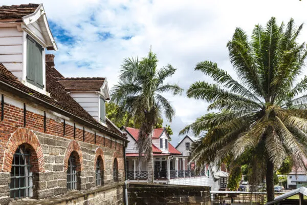 Bakstenen muur en gebouwen van het historische Fort Zeelandia, omgeven door palmbomen onder een licht bewolkte lucht in Paramaribo.