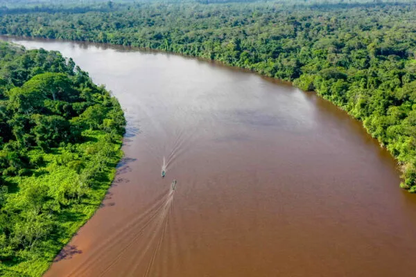 Panoramisch bovenaanzicht van de brede, bruine Surinamerivier nabij Atjoni, meanderend door het dichte, ononderbroken groene tropische regenwoud met een paar kleine bootjes op het water.