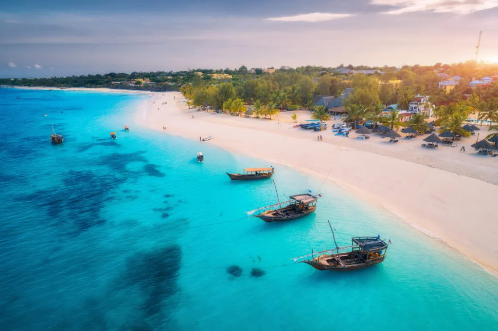 Traditionele houten vissersboten drijven op de helderblauwe oceaan langs een goudgeel zandstrand op Zanzibar in Tanzania.
