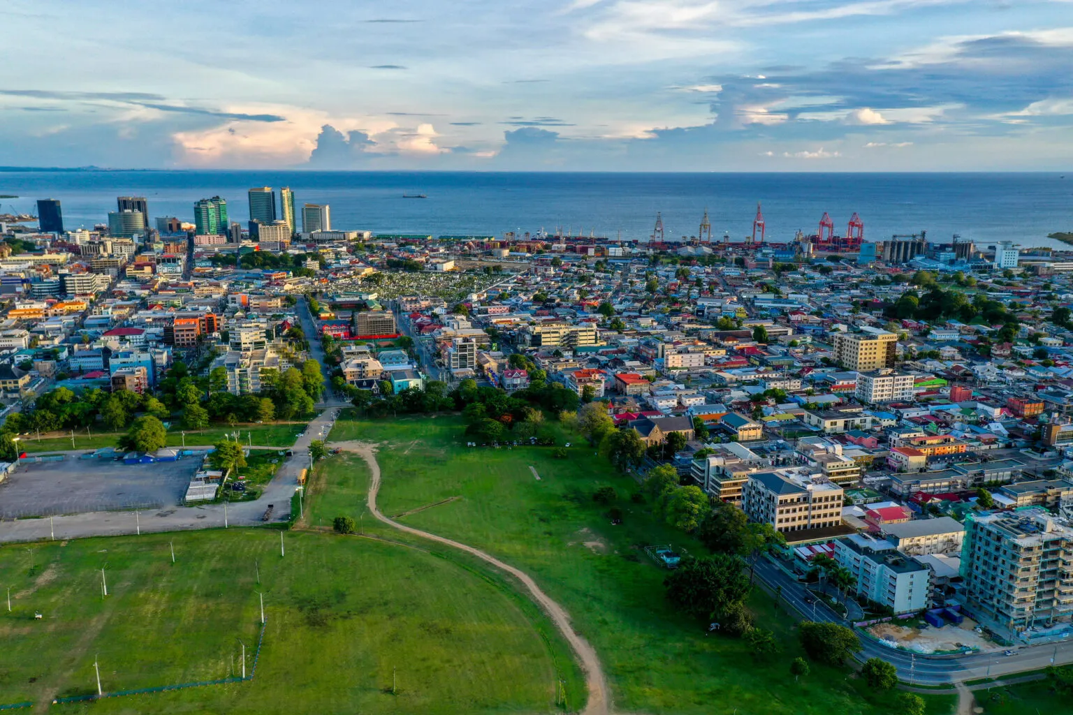 Panoramisch luchtfoto-overzicht van Port of Spain met het groen van Queen's Park Savannah op de voorgrond, de stad met hoogbouw en de zee aan de horizon op Trinidad.