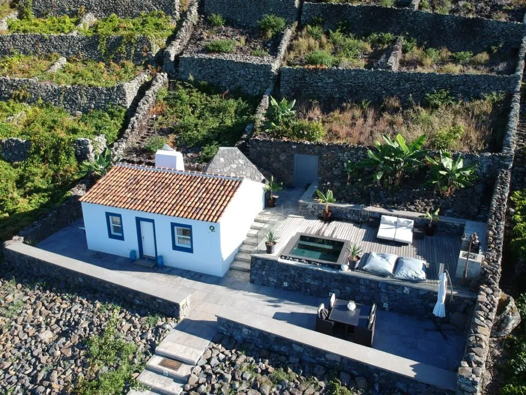 Bovenaanzicht van het witte vakantiehuis Vigia da Areia met een oranje dak, terras en omliggende groene terrassen op Santa Maria in de Azoren.