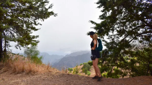 Een vrouw met een rugzak staat tussen de bomen op een bergpad en kijkt uit over de vallei bij Caibros op Santo Antão, Kaapverdië.