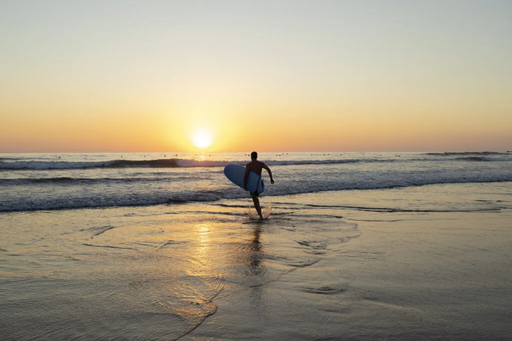 Silhouet van een surfer die met een surfplank onder de arm het water in rent op het strand van Jeffreys Bay, Zuid-Afrika, tijdens een gouden zonsondergang.