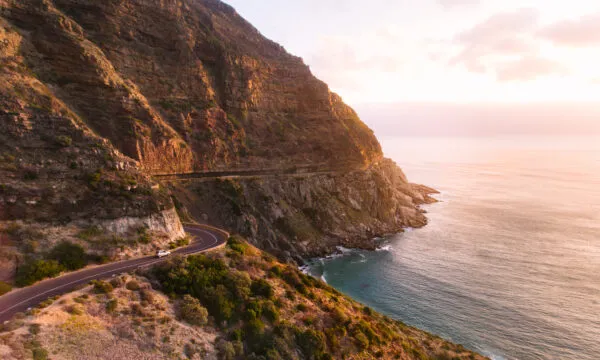 Een slingerende autoroute langs steile bergkliffen met uitzicht op de oceaan tijdens zonsondergang nabij Kaapstad, Zuid-Afrika.