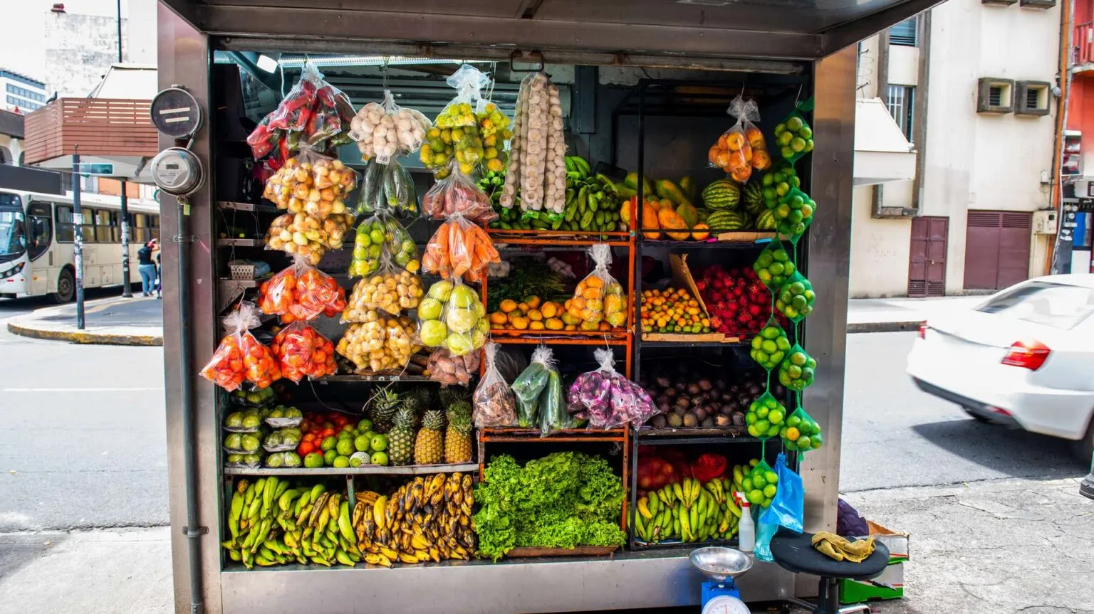 Een overvolle marktkraam in Costa Rica, gevuld met kleurrijke schappen vol vers fruit, bananen, groenten en zakjes met producten.