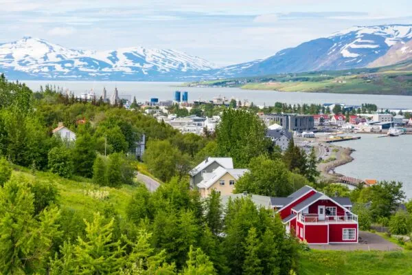 Uitzicht over de stad Akureyri, het Eyjafjörður-fjord en groen begroeide heuvels met op de achtergrond met sneeuw bedekte bergen in IJsland.