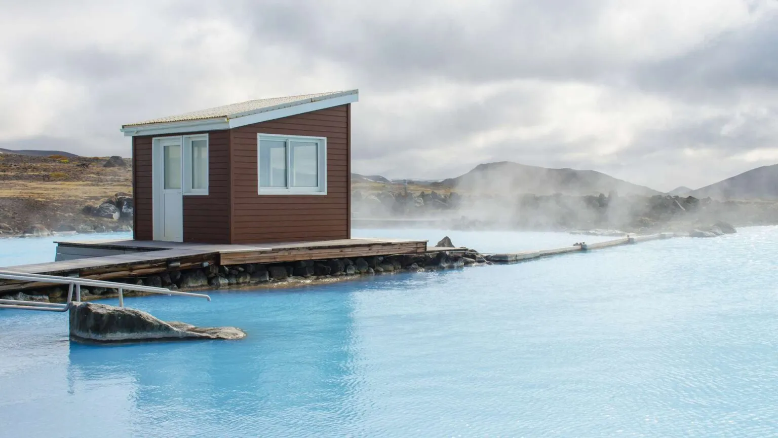 Een klein bruin houten gebouw op een steiger aan het melkblauwe, stomende water van de Blue Lagoon in IJsland.