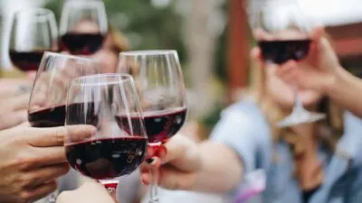 Een groep vrienden brengt een proost uit en houdt glazen gevuld met rode wijn bij elkaar in de buitenlucht.