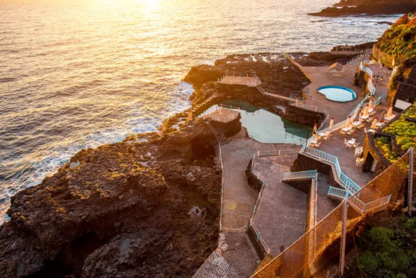 Natuurlijke zwembaden van Charco Azul aangelegd in de rotsen aan de oceaan, verlicht door het warme gouden licht van de zonsondergang op La Palma.