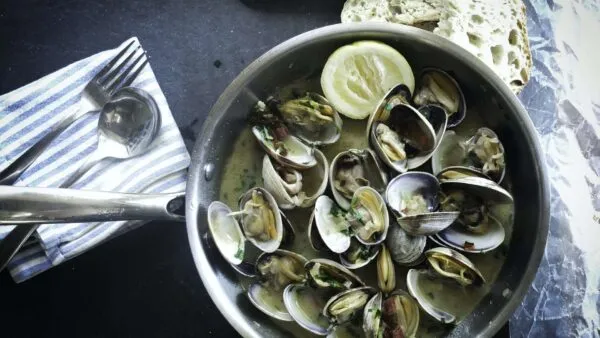 Een metalen pan gevuld met bereide schelpdieren in saus en een schijfje citroen, geserveerd met brood en bestek op Madeira.