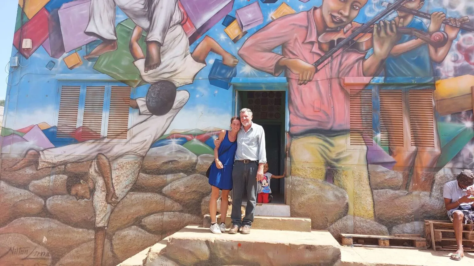 Frei en Sofie staan arm in arm voor een kleurrijke muurschildering bij het project Espaço Jovem in Mindelo op São Vicente.