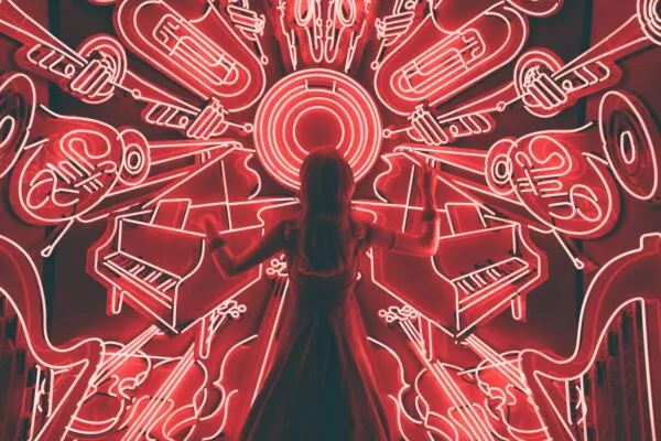 Het silhouet van een dirigent op de rug gezien voor een opvallende, rood verlichte neonmuur vol verschillende muziekinstrumenten.