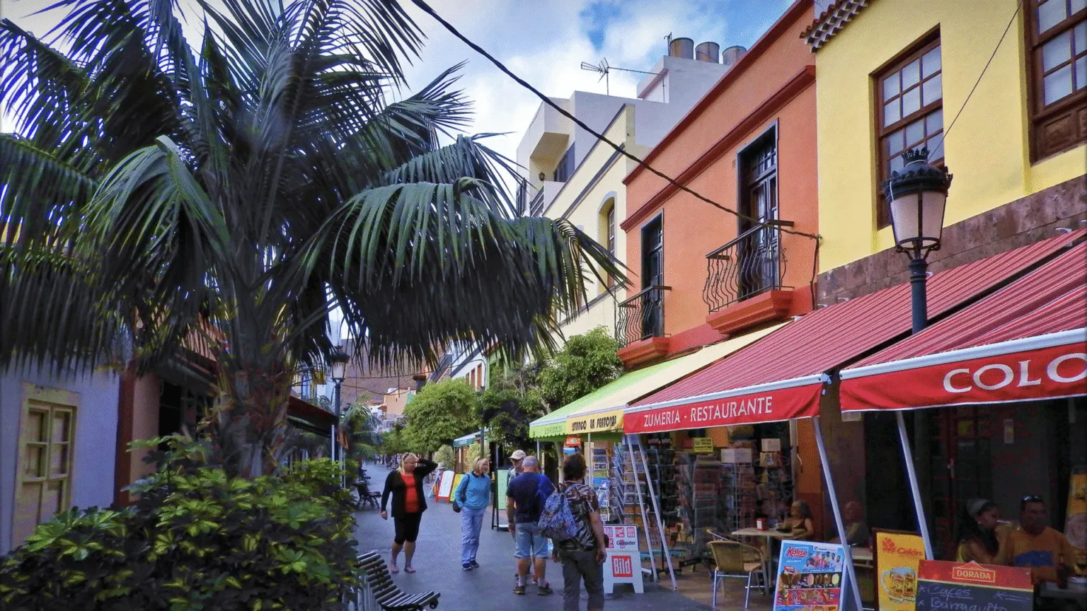 Een sfeervolle voetgangersstraat met kleurrijke gevels, luifels van lokale winkels en palmbomen in San Sebastián de La Gomera.