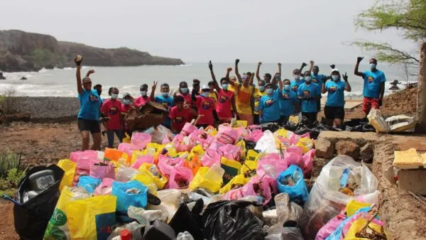 Een groep enthousiaste vrijwilligers zwaait achter een grote stapel verzamelde zakken afval op het strand tijdens World Cleanup Day op Boa Vista.