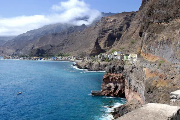 Een steile rotsachtige kustlijn met een kustweg die langs de kliffen slingert naar een kustdorp op het eiland Santo Antão, Kaapverdië.