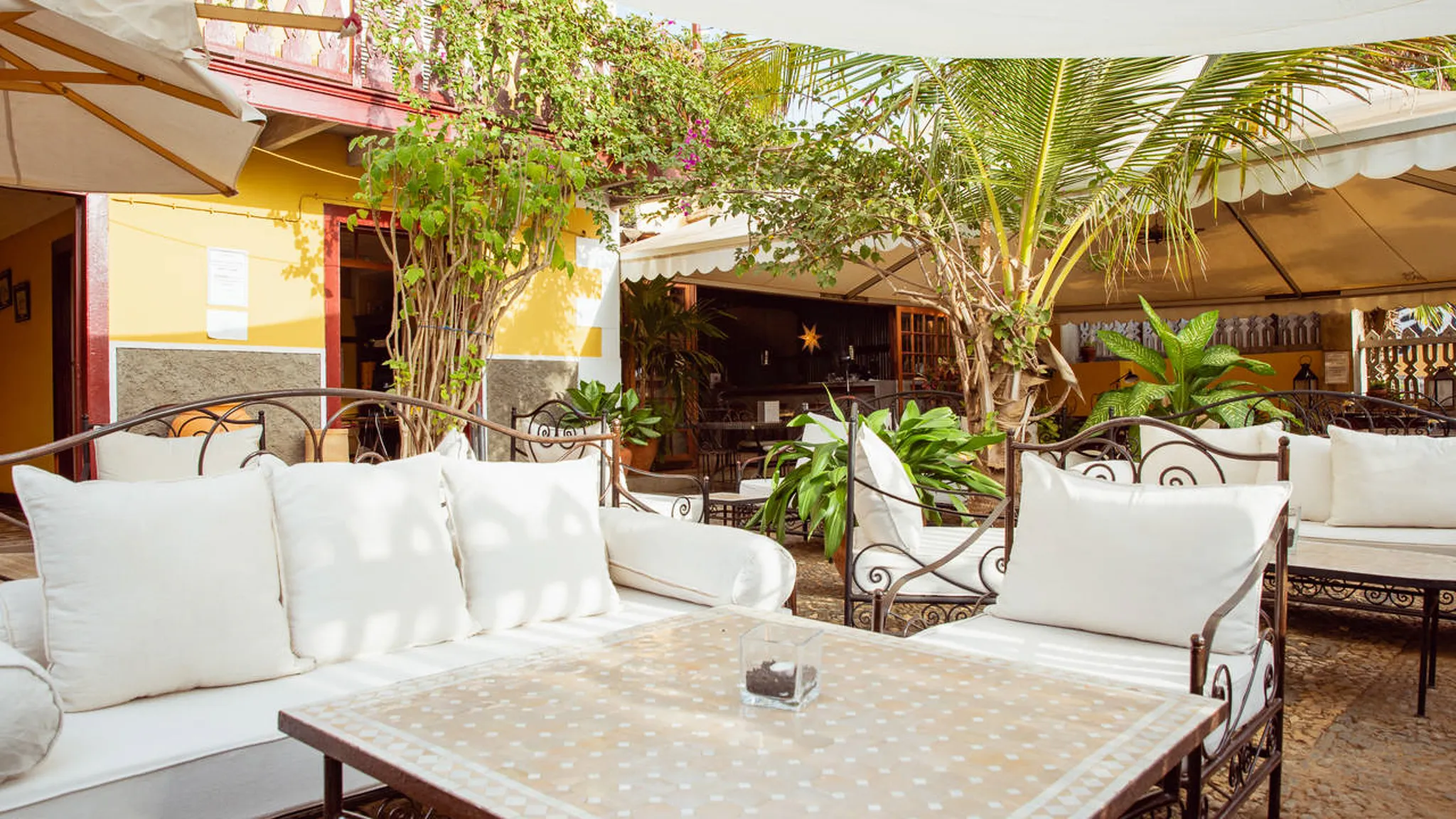 Het overdekte terras van Vince & Luisa's Boetiekhotel, met groene beplanting en uitnodigende banken en stoelen met dikke witte kussens