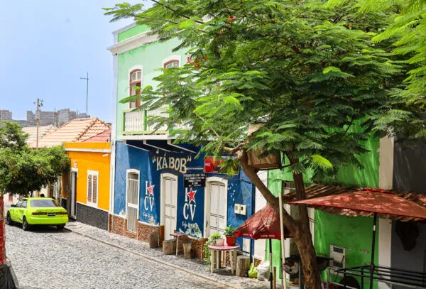 Een straatbeeld van São Filipe met vrolijk gekleurde blauwe en groene gebouwen, een lokale winkel en een klinkerstraatje op Fogo.