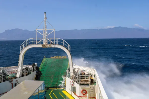 Uitzicht vanaf de boeg van een ferry die door het wilde blauwe zeewater vaart met opspattend water en de bergen van Santo Antão op de achtergrond in Kaapverdië