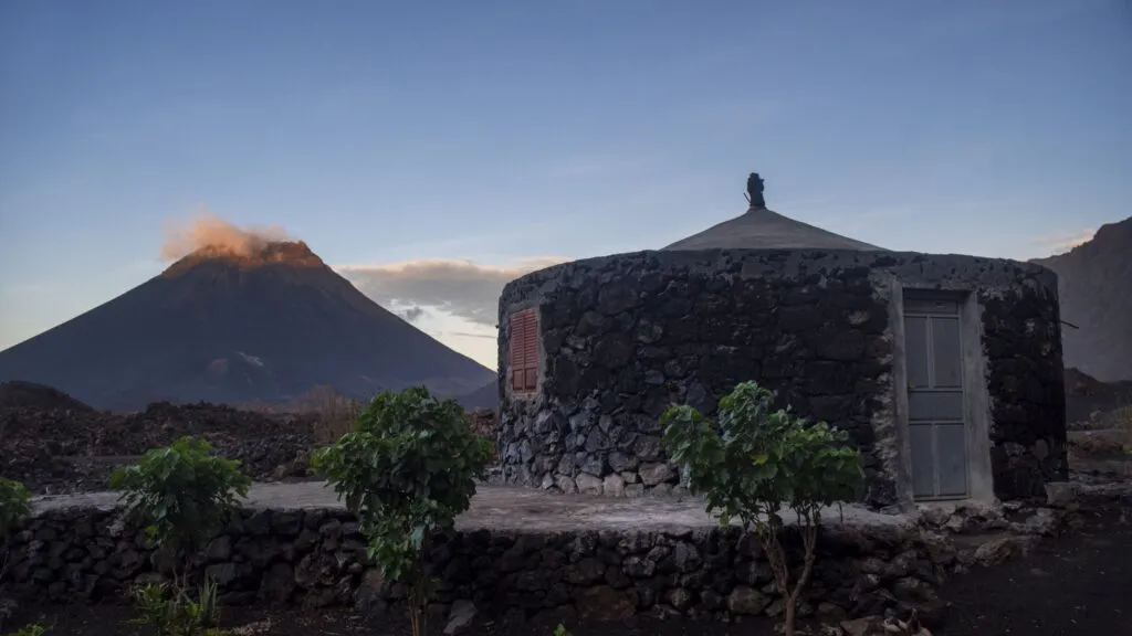 Een funku, lavastenen huisje, met de Pico do Fogo op de achtergrond tijdens avondschemer