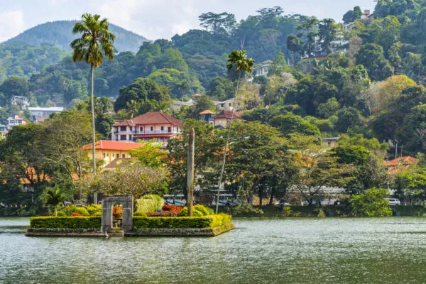 Zicht op het centrale eilandje in Kandy Lake omringd door water, met op de achtergrond traditionele gebouwen en dichtbegroeide groene heuvels.