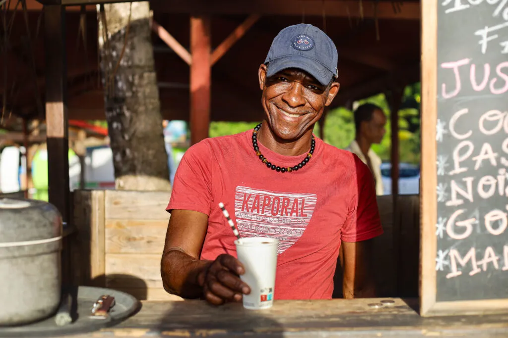 Portret van een glimlachende lokale man met een drankje bij Plage de Malendure in Guadeloupe.