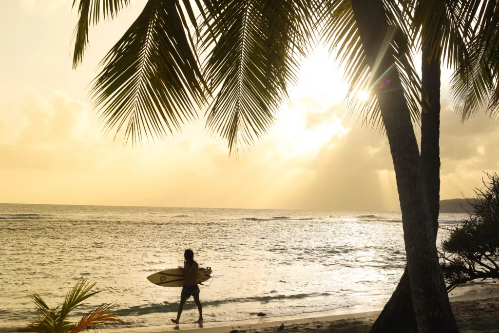 Een surfer met een surfplank langs de waterkant op het strand van Sainte-Anne, Guadeloupe.