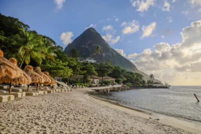Uitzicht op het witte zand van Sugar Beach met rieten parasols, de blauwe baai en een van de beroemde Pitons op de achtergrond