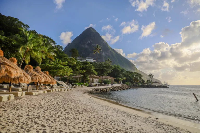Uitzicht op het witte zand van Sugar Beach met rieten parasols, de blauwe baai en een van de beroemde Pitons op de achtergrond