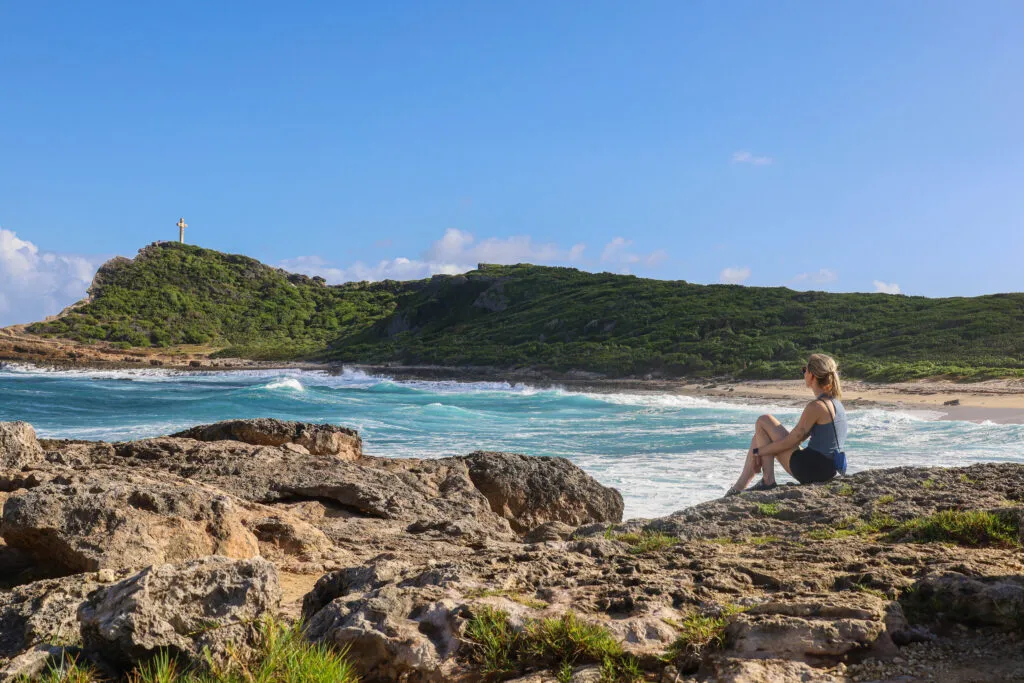 Een vrouw zit op de rotsachtige kust van Pointe des Châteaux in Guadeloupe en kijkt uit over de turquoise zee.