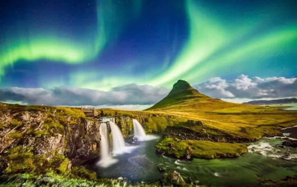 Groen noorderlicht danst aan de nachtelijke hemel boven de iconische berg Kirkjufell en de Kirkjufellsfoss waterval op het schiereiland Snæfellsnes in IJsland.