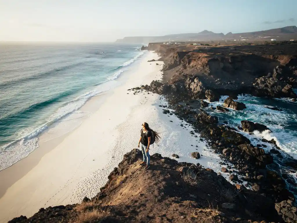 Reiziger op klif met uitzicht op turquoise Caribisch strand en vulkanische Cape Verdische kustlijn tijdens gouden uur.