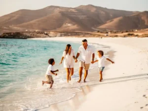 Gezin met jonge kinderen spelend in turquoise Atlantisch water op een wit vulkanisch strand in Kaapverdië.