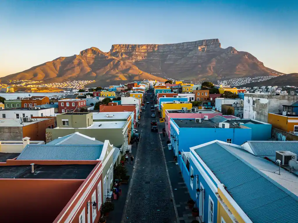 Kleurrijke pastelhuizen in Bo-Kaap, Kaapstad, met kasseienstraatjes en de vlakke top van de Tafelberg op de achtergrond.