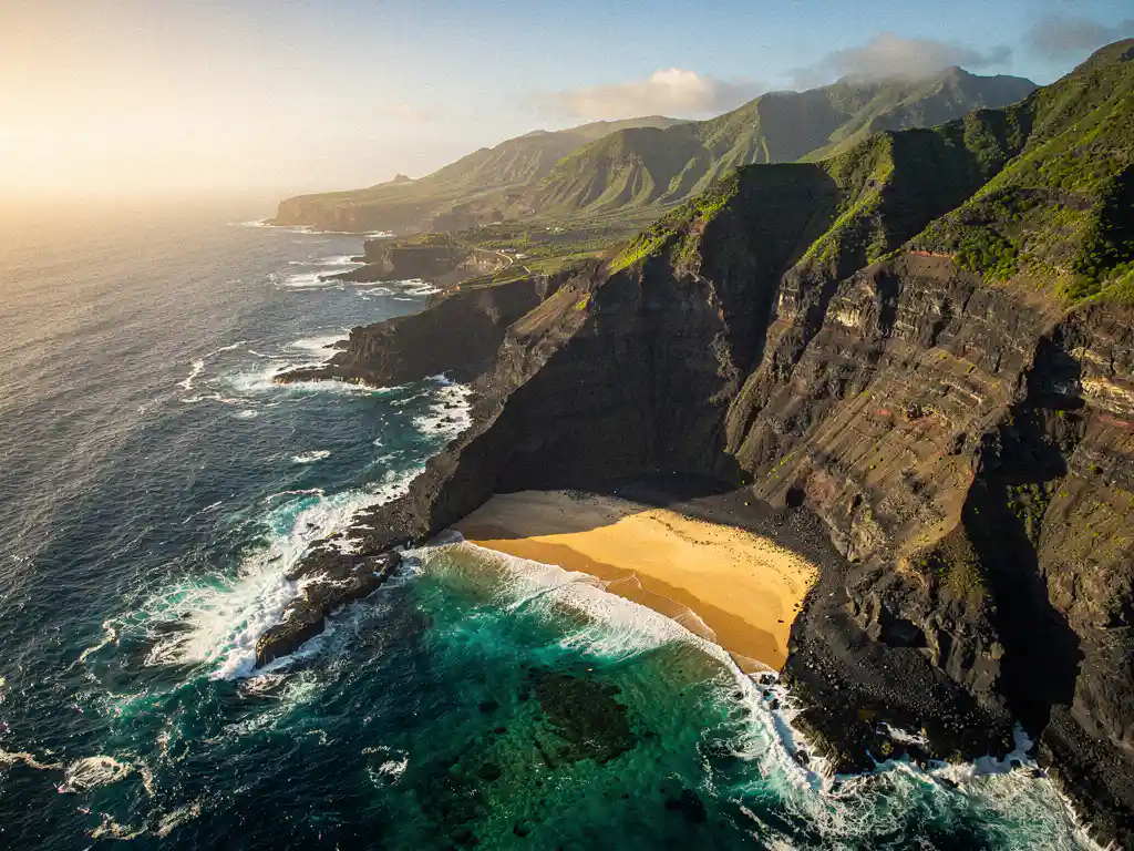 Luchtfoto van een vulkanische kustlijn op Kaapverdië met zwarte lavakliffen, turquoise Atlantische golven en een gouden zandstrand in een beschutte baai.